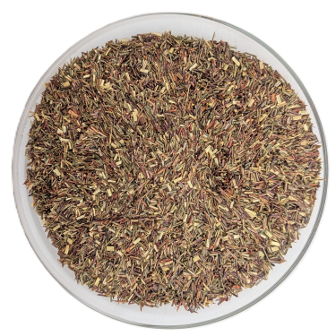 Draufsicht auf eine runde Glasschale, gefüllt mit losem, grünem Bio-Rooibos-Tee. Die feinen Tee-Nadeln zeigen eine Mischung aus grün-gelben und leicht rötlichen Nuancen auf rein weißem Hintergrund.