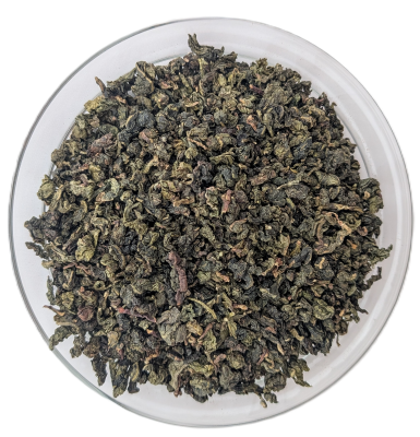 Ti Guan Yin Oolong Tee – eng gerollte, dunkelgrüne bis bräunliche Teeblätter in einer transparenten Schale von oben fotografiert.