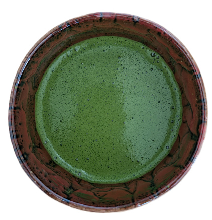 Vogelperspektive auf eine traditionelle Keramikschale mit frisch aufgeschlagenem, feinschaumigem Matcha-Tee in kräftigem Grün.