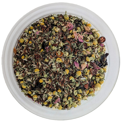 Eine runde Glasschale, von oben fotografiert, gefüllt mit einer sehr detailreichen Teemischung. Die Basis besteht aus feinen, rötlich-braunen Rooibos-Nadeln und grünen Kräutern. Darunter mischen sich zahlreiche kleine, intakte gelbe Kamillenblütenköpfe so