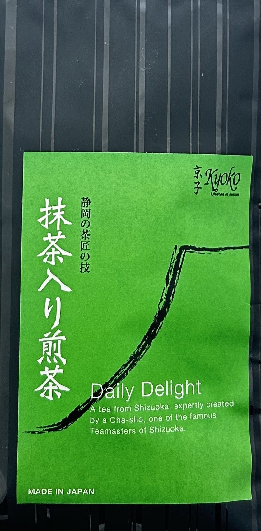 Moderne, matte Teeverpackung mit einem großen, minimalistischen Etikett in sattem Dunkelgrün. Das Etikett zeigt den Markennamen Kyoko und den Produktnamen Daily Delight in klarer weißer Schrift, ergänzt durch traditionelle japanische Schriftzeichen. Am un