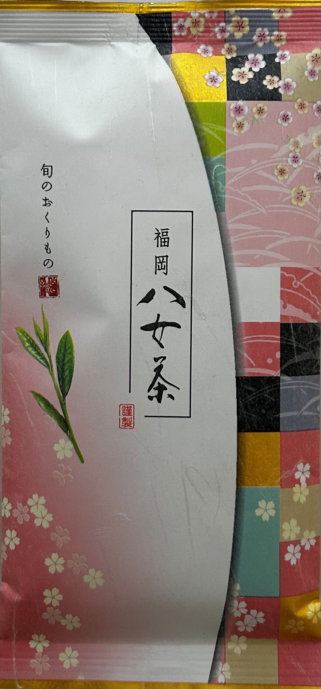 Ästhetische japanische Teeverpackung, die am rechten Rand ein kunstvolles Patchwork-Muster aus rosa und bunt karierten Quadraten zeigt, kombiniert mit zarten, fallenden Kirschblüten (Sakura). Auf der linken, weißen Seite ist eine filigrane Grafik von drei