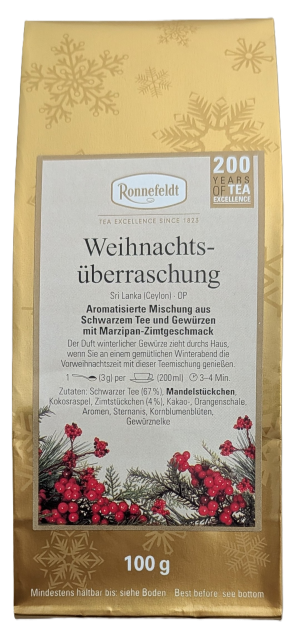 Goldene 100g-Tüte des Ronnefeldt Schwarztees Weihnachtsüberraschung mit festlichem Etikett und Schneeflockenmuster.