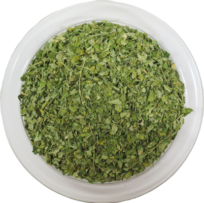 Eine runde Glasschale aus der Vogelperspektive, gefüllt mit fein geschnittenen, getrockneten Moringa-Blättern. Die gleichmäßig grünen Blattstücke haben eine zarte Textur.