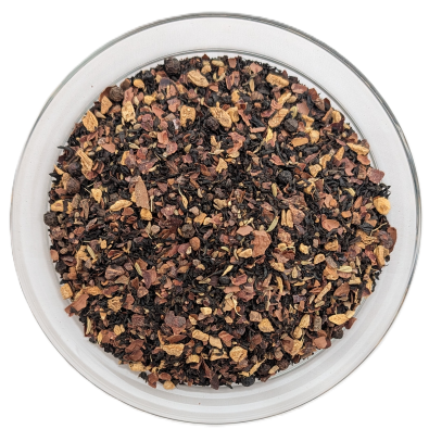 Schwarzteemischung Schoko Chai in einer klaren Schale mit dunklem Tee, gebrochenen Kakaoschalen, braunen Gewürzen und schwarzen Pfefferkörnern.