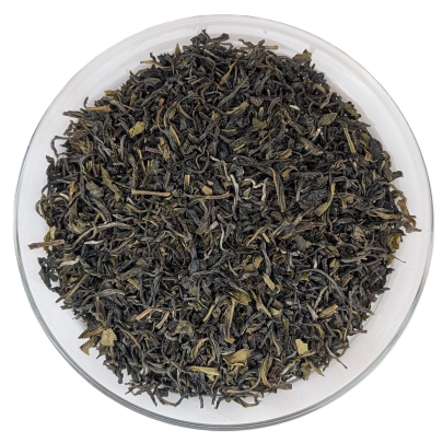 Trockener Bio Darjeeling Risheehat Tee mit gedrehten, dunkelgrünen und braunen Blättern sowie hellem Tips-Anteil in einer Glasschale.