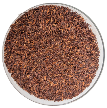 Draufsicht auf eine runde Glasschale, gefüllt mit losem, fermentiertem Bio-Rooibos-Tee. Die fein geschnittenen Nadeln haben eine durchgehende, warm-rotbraune Färbung auf rein weißem Hintergrund.