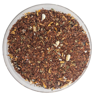Lose Rooibos-Tee-Mischung mit kleinen bunten Zuckerstreuseln, getrockneten Apfelstücken und Kakaoschalen, serviert in einer klaren Glasschale auf weißem Hintergrund.