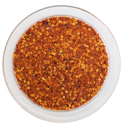 Draufsicht auf eine runde Glasschale vor weißem Hintergrund, befüllt mit einer groben Harissa-Mischung, die von zahlreichen gelblich-beigen Chilikernen und intensiv roten Chiliflocken dominiert wird.