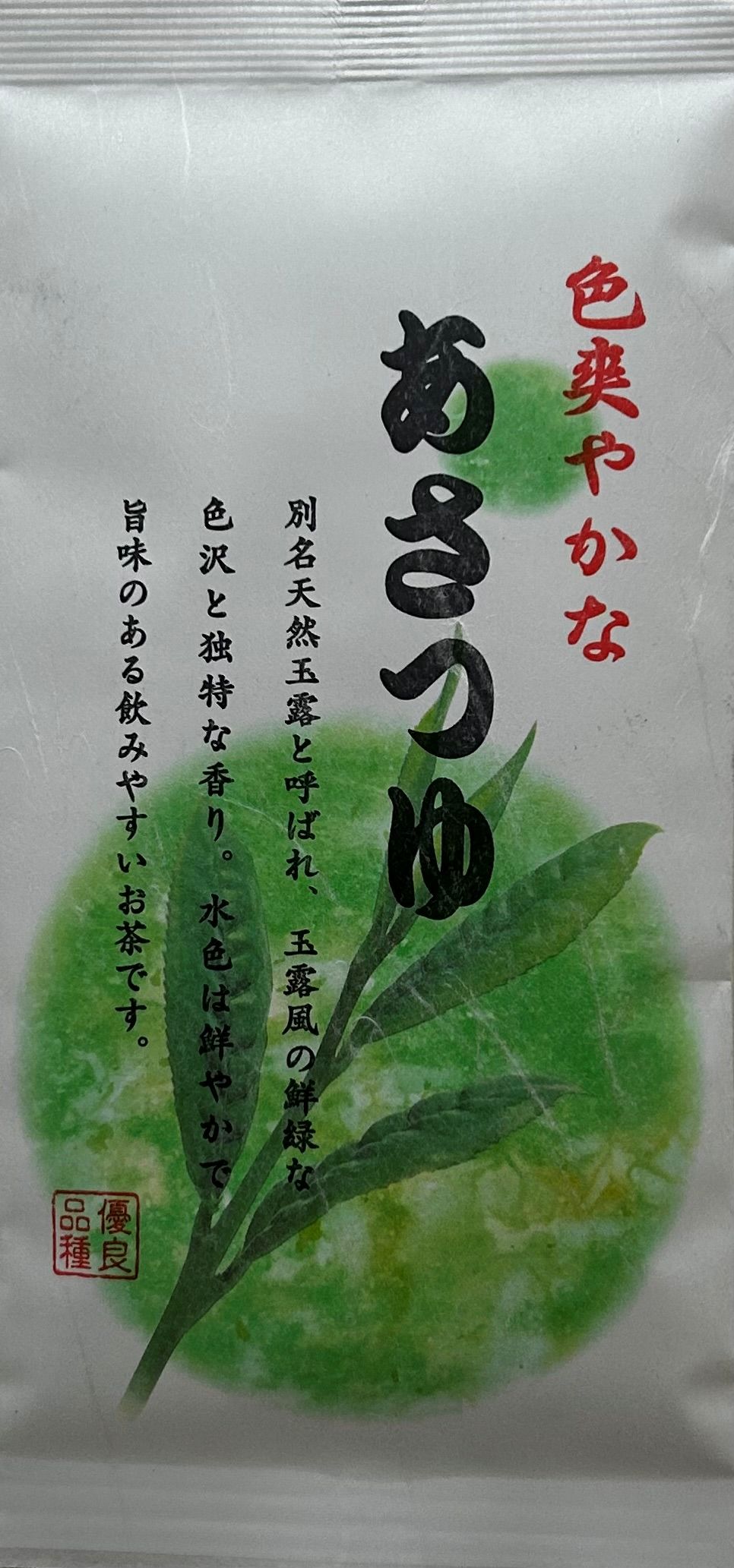 Weiße Teeverpackung für japanischen Asatsuyu Grünen Tee mit einer Illustration von grünen Teeblättern vor einem runden, grünen Hintergrund und japanischen Schriftzeichen.