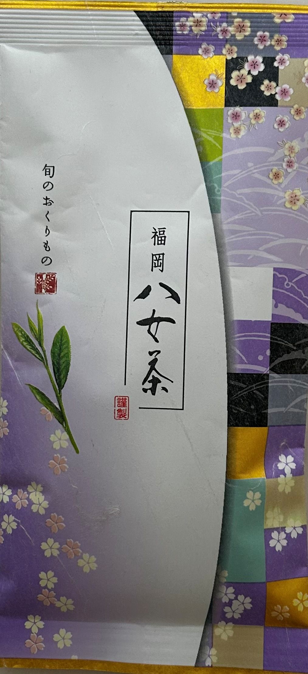 Kunstvolle japanische Teeverpackung für den Sencha Shizuku No. 1. Das Design ist dynamisch geschwungen und zweigeteilt: Die rechte Seite besticht durch ein traditionelles, buntes Patchwork-Muster im Chiyogami-Stil aus lila, grünen, schwarzen und goldenen