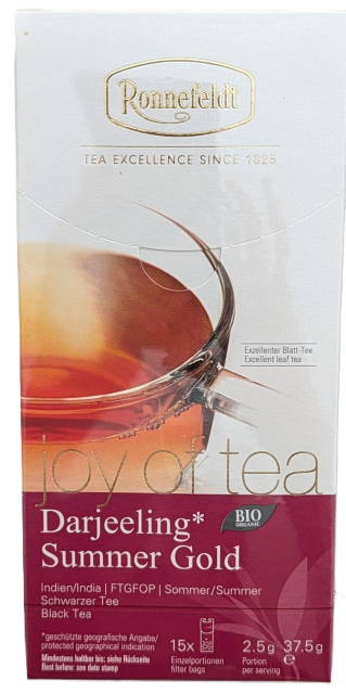 Die Verpackung von Ronnefeldt Joy of Tea "Darjeeling Summer Gold". Oben weiß mit goldenem Ronnefeldt-Logo und einer Abbildung einer gefüllten Glastasse. Die untere Hälfte ist beere/weinfarben mit weißer Aufschrift: "joy of tea®", "Darjeeling* Summer Gold"