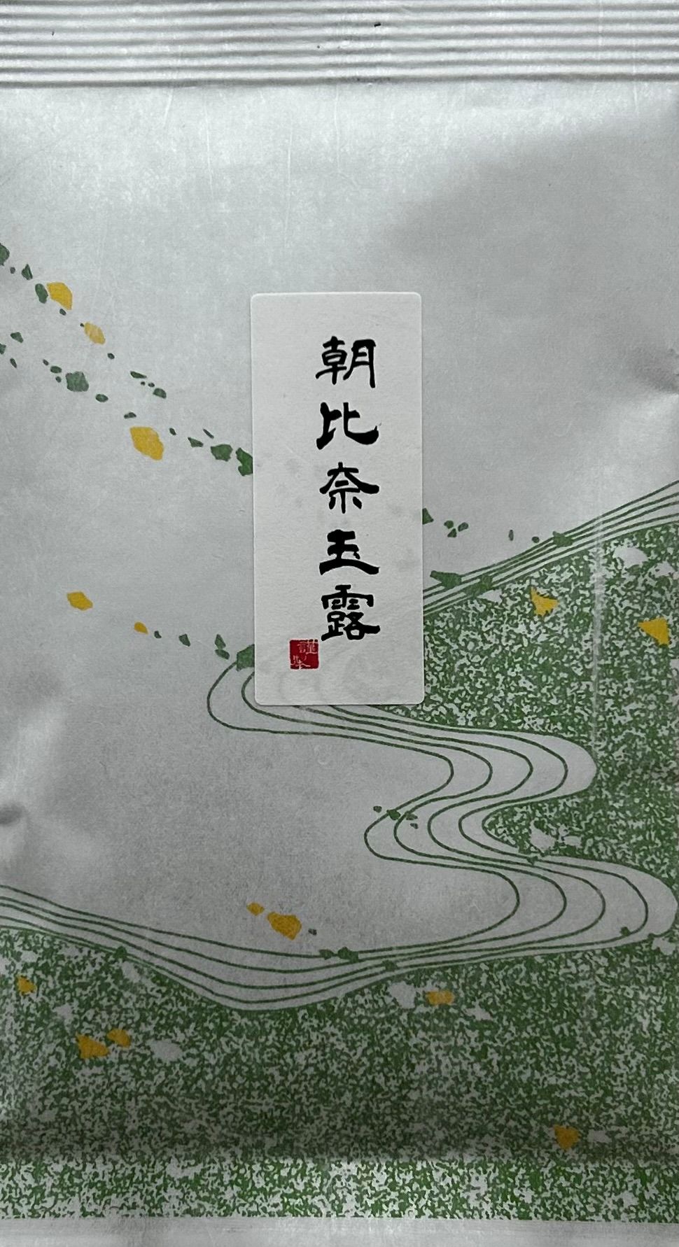 Traditionelle japanische Teeverpackung aus hochwertig strukturiertem, weißem Washi-Papier mit fühlbarer Faseroptik. Die untere Hälfte ist mit einem eleganten, wellenförmigen Muster in verschiedenen Grün- und Weißtönen verziert, das an klassische Meereswel