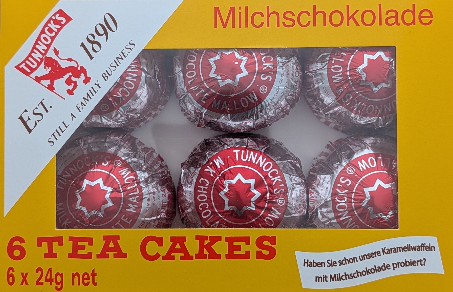Die gelbe Vorderseite einer Packung Tunnock's „6 Tea Cakes“. Durch ein Sichtfenster sind sechs rundliche, in glänzende rot-silberne Folie gewickelte Schaumküsse erkennbar. Oben rechts ist das weiße Markenlogo mit einem roten Löwen zu sehen, links steht de